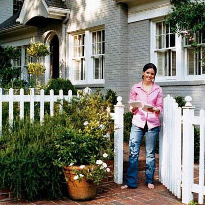 युवा homeowner in front of her painted brick house with a white picket fence in front