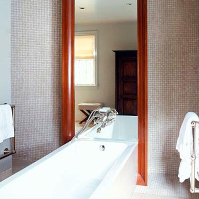 मंज़िल to ceiling framed mirror rests on the wall behind a modern, sleek, white bath tub