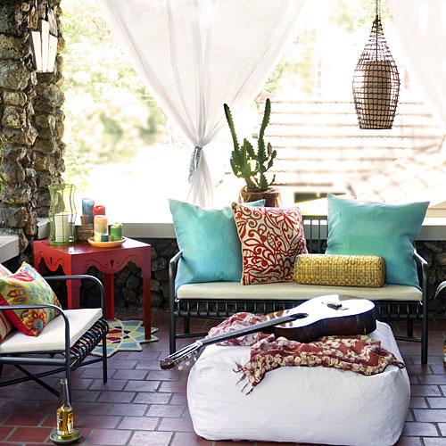 सामने porch with porch furniture (love seat and chairs with white cushions, colorful, red side table and a white bean bag in the middle with a guitar on top)
