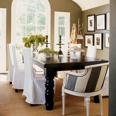 klasik and stylish dining room with a large black table with white, slip-covered chairs surrounding it and a striped arm chair at the head of the table