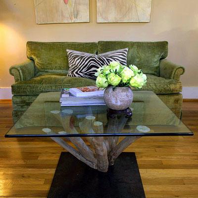 कॉफ़ी table made out of the base of a crepe myrtle with a glass top facing in front of a green couch with a zebra pillow 