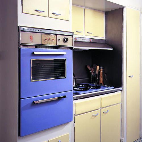 में this kitchen update, periwinkle paint covers a kitchen oven and stovetop while the cabinets’ doors are painted a pale yellow color with rest covered in creamy white.