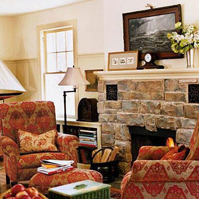 विशाल, natural stones around the hearth update this fireplace's style while red and tan velvet fabric decorates the arm chairs that are placed on either side.