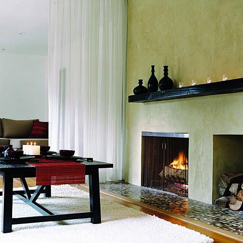 चिकना, stucco-covered fireplace with a dark wood mantel and a storage place for a stack of wood in this lounge space