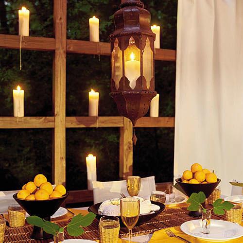 सफेद candles are placed on the wooden ledges surrounding the deck with a table decorated with lemons in bowls, a hanging lantern, white plates and wine glasses