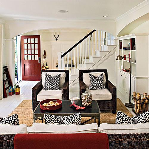 काली and white graphic print plush cushions are arranged in the living room's wicker arm chairs while white walls brighten up the overall lighting of the living room