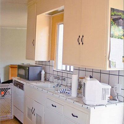 keittiö with peach cupboards above the sink and white cupboards below with white tile backsplash and tile counters