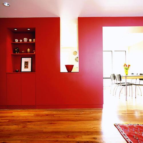 दीवारों in this living room are saturated with deep red hues and inset, built-in shelving accents accessories and a framed painting